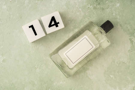 Bottle of cologne and number fourteen on green with copy space. bottle with blank lable