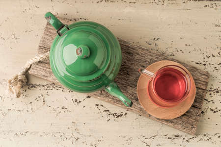 a glass of tea and green enamel teapot on a wooden table