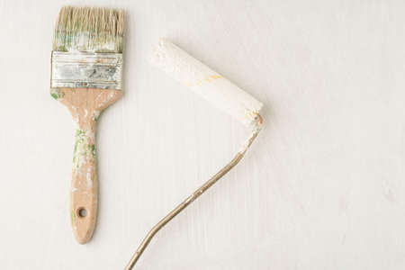 an used dirty paint brush and roller on a white wooden backfround with copy space