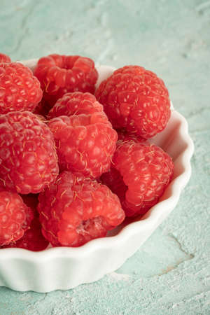ripe red raspberry fruits in a bowl on green textured background with copy space