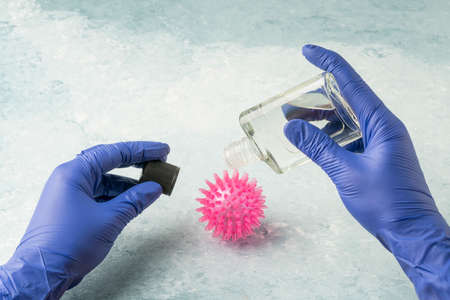 hand in latex gloves pouiring anticeptic cologne onto corona virus modelの写真素材