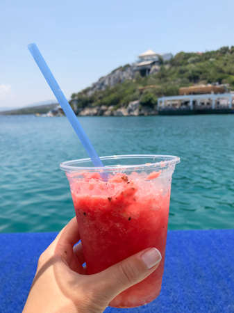 a female hand holding a glass of watermelon cocktail in summer against the sea