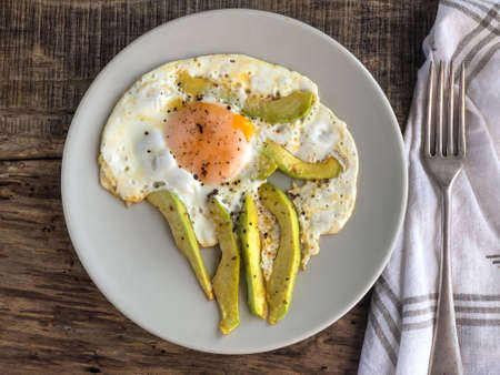 closeup fried egg with avocado slices on plate on the wooden table for breakfastの写真素材