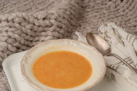 bowl of pumpkin soup on a white tray on the bed covered with blanket in winterの写真素材