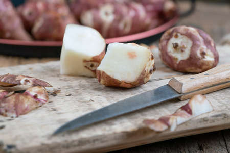 Pealed and halved Jerusalem artichokes on wooden cutting board to preparing food. raw tuber root...