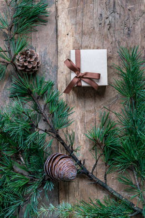 Christmas present box, fir or christmas tree branch and pine cones on wooden background. Top view gift box on wooden surface with copy space for christmas or new yearの写真素材