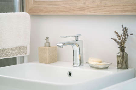 bathroom, hanged towel and liquid soap bottle by white sink in domestic bathroom at home interior. faucets and soaps on white and clean sink in domestic toilet with selective focus and noise effectsの写真素材