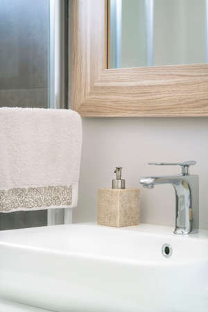 bathroom, hanged towel and liquid soap bottle by white sink in domestic bathroom at home interior....