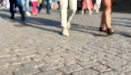 walking, Blurred background with feet of women and men walking on cobblestone road or pavement with copy space in a sunny day. city life concept background or surface with feet of people on streetの写真素材