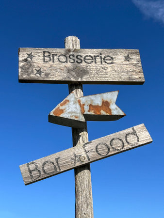 direction sign, old wooden sign board for bar and food with rusty direction arrow over beautiful blue sky with selective focus in a sunny day. wooden board with brasserie and bar sign on over skyの写真素材