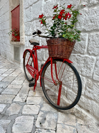 bicycle, red bike or bicycle with beautiful flowers in its basket parked leaning against the white stone wall of a house or home in a narrow street in Europe. transportation concept photo.の写真素材