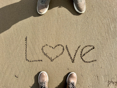 love, hand written love word on sand. female and male feet standing on a sandy beach. romance on beach. romantic relationship conceptの写真素材