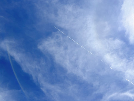 sky, beautiful blue sky with dory white clouds and trace line of a plane flying in the air. natural background or surface with white clouds in a sunny dayの写真素材