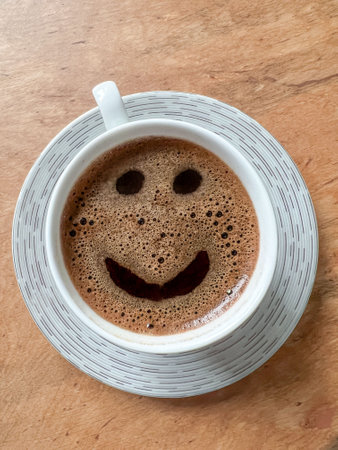 coffee, top view beautiful cup of greek or turkish coffee with smile face icon on wooden table or background. happy or funny moments in a cafe. hot drink or beverage concept with smiling face iconの写真素材