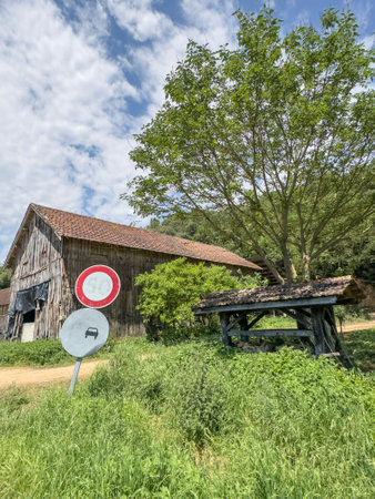 road sign, old damaged road signs in front of wooden hut house or home in a rural area or countryside in a sunny day. old abandoned wooden house and its garden under blue sky. tree by hut by pathの写真素材