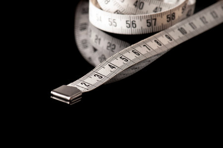 measure tape, dieting or weight loss theme, isolated on black background with reflection and copy...