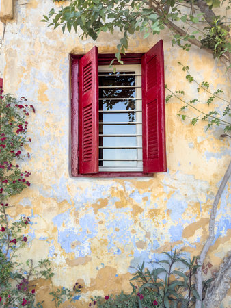 window, side view window with wooden red blinds or shutters on old textured wall with flowers. building exterior with copy space. old house or home background or surfaceの写真素材