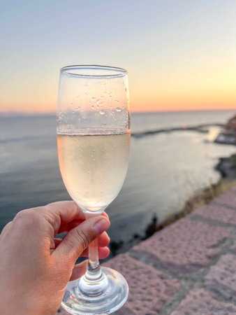drink, Hand Holds Sparkling Champagne wine Glass at Sunset by Sea. Sparkling wine in elegant champagne flute over golden seaside sunset, romantic drink moment with soft evening light with copy spaceの写真素材