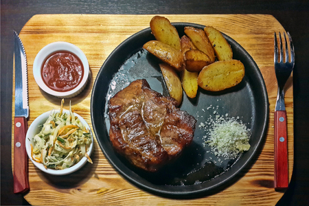 Pork steak in a skillet with red sauce and salad, served on a board, with cutlery.の写真素材