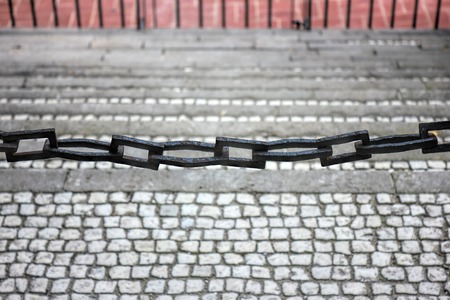 Focus point is on the metal chain fence. Gray cobblestone on the background.