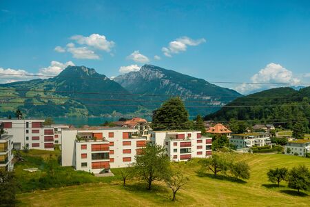 Scenic view from the train to the valley in Switzerland. Small town and lake, green mountains in Switzerland. Beautiful nature in summer sunny dayの写真素材