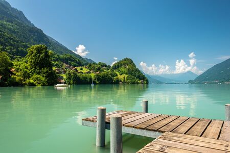 View of Brienz lake with clear turquoise water. Wooden pier. Traditional wooden houses on the shore of Brienz lake in the village of Iseltwald, Switzerlandの写真素材