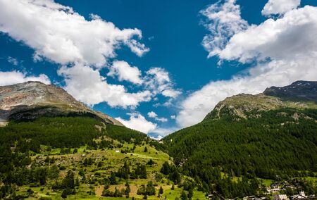 A small village with a church in the Swiss Alps. View of the green slope in the mountains. Idyllic outdoor scene in Switzerland, Europeの写真素材