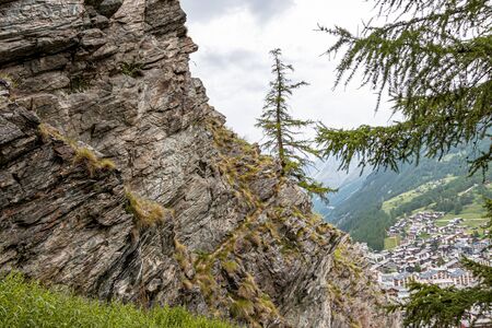In the foreground a sheer cliff, in the background you can see the houses of the mountain resort Zermatt, Switzerland.の写真素材