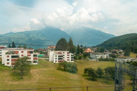 view from the train window. A train passes by residential buildings, in a distant mountain in clouds and haze.の写真素材