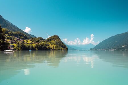 View of Brienz lake with clear turquoise water. Sailing boats. Traditional wooden houses on the shore of Brienz lake in the village of Iseltwald, Switzerlandの写真素材