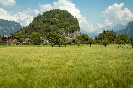 Idyllic landscape in the Alps with fresh green meadows, typical farmhouses and snowcapped mountain tops in the backgroundの写真素材