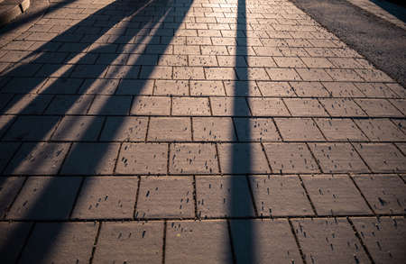 Abstract shadows of people walking in a street of the city. The sidewalk is sprinkled with granite...
