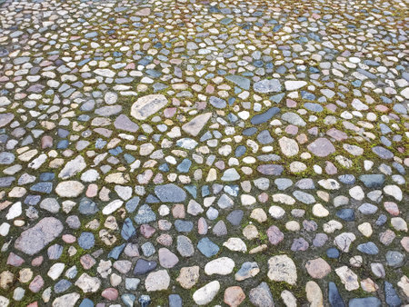 Cobblestone street with grass between the stones, multi-colored cobblestones, rubble masonry, texture or backgroundの写真素材