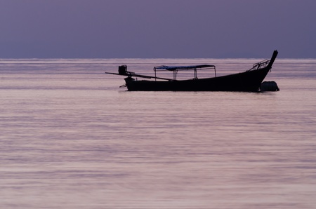 Silhouette of a longtail boat in the sea at sunrise.