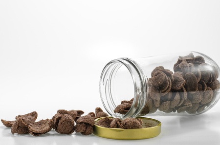 Chocolate cereal spill out from an open glass bottle , photograph on white background.