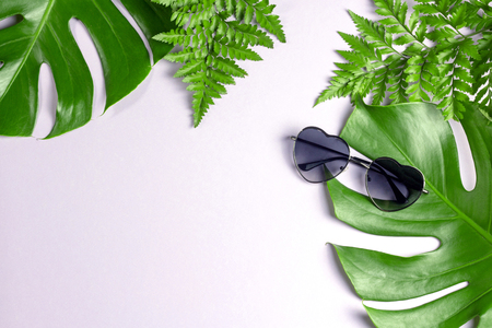 Tropical split leaves and fern with heart shaped sun glasses on pastel pink backgroundの写真素材