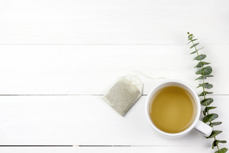 Morning tea cup with Eucalyptus Silver Dollar plant leaves on white wood panel backgroundの写真素材