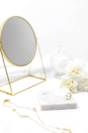 White women cosmetic desk decorated with marble white fabric golden round mirror ring necklace and...