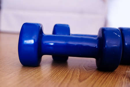 fitness weights dumbbells for exercise concept. Exercise and fitness equipment at home for basic work out with blue dumbbells and wooden backgroundの写真素材