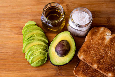 fresh and sliced avocado, salt, oil and bread on wooden background top view close-upの写真素材