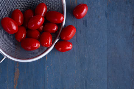 fresh cherry tomatoes in a colander with blue wooden background, top view, copy spaceの写真素材