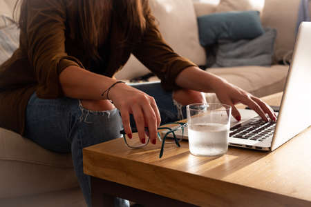 home work space - work from home concept - girl working or studying with a laptop sitting on a sofa by a wooden deskの写真素材