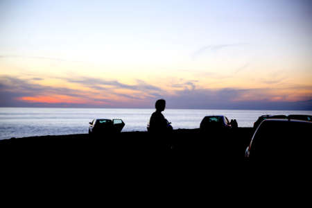 silhouette of a young girl walking at sunset in a car park, camping scene, summer context, light backgroundの写真素材