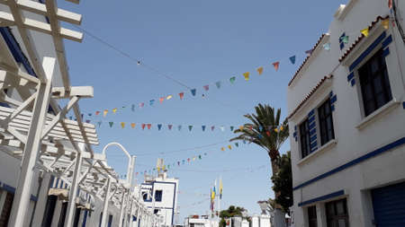 pretty little town with little white and blue houses decorated with festive garlands hanging in the streets. Colorful flags garland decoration. Agaete, Gran Canariaの写真素材