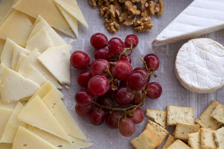 Cheese board with different types of sliced and soft cheese, grapes, bread and nuts. cheese plate top view with white backgroundの写真素材