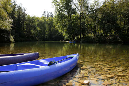 canoes or kayaks on the bank of a beautiful river with a background of trees and kayaks descending the river. sport and nature context. Sella river, Spainの写真素材