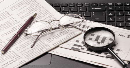 glasses and old newspaper lying on the black open laptop