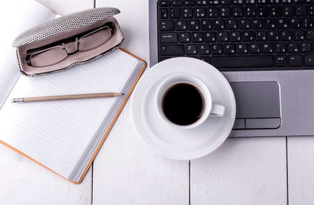 laptop, notebook with a cup of coffee and a pencil lying on a wooden table. Top view