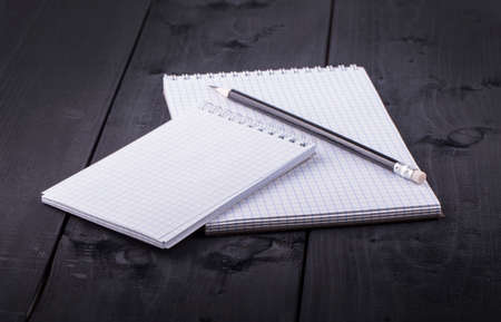 Pencil and notepad with spiral on black wooden textured table. Side view.
