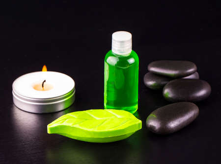 Composition of spa treatment on wooden background. Soap, candle, bottle of oil and spa stones on black table.の写真素材